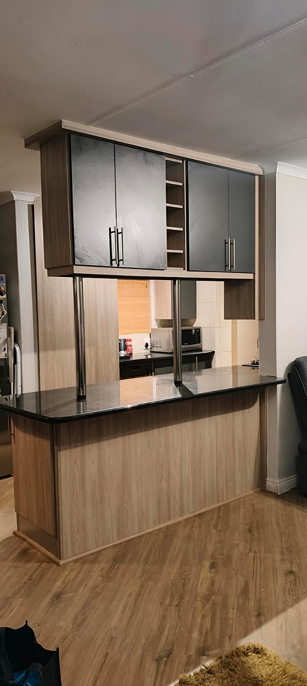 Custom kitchen and bar counter renovation featuring floating dark wood upper cabinetry, granite countertops, and stainless steel support poles by Revival Space.