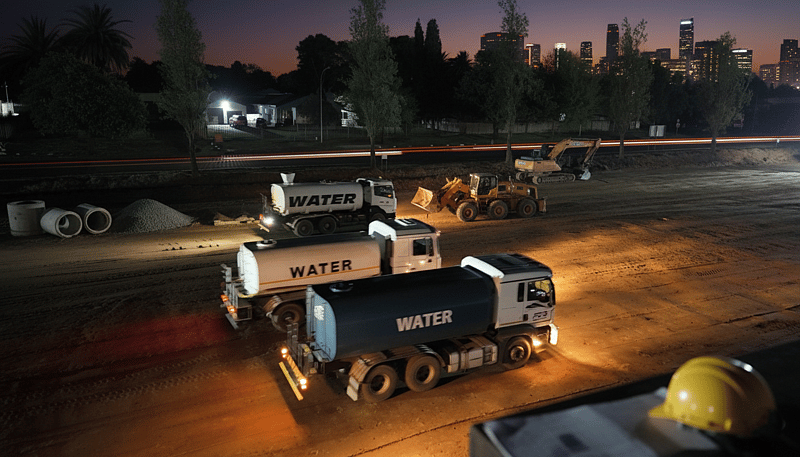 Multiple Aquafleet water trucks working on a large site at dusk